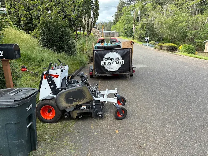 Coos Coast Cleanup branded equipment trailer and Bobcat compact loader on a Coos County road