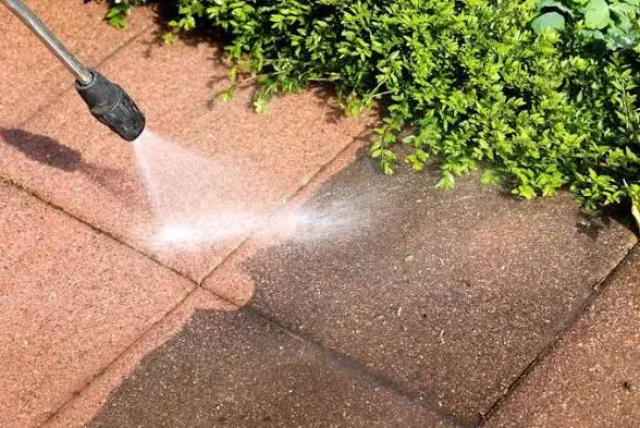 Pressure washer lifting grime off a paved patio surface, leaving a clean stripe